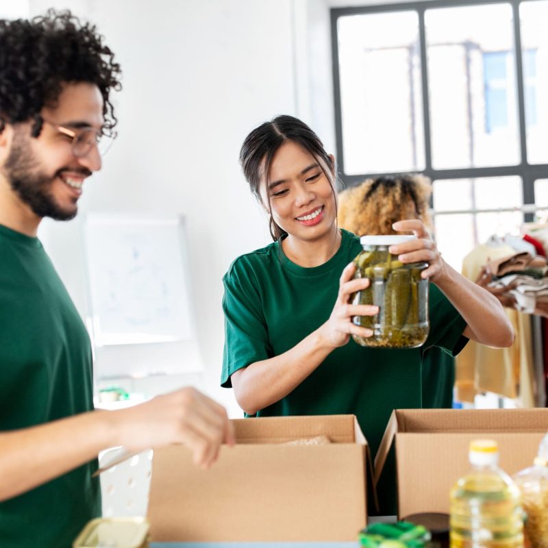 charity, donation and volunteering concept - international group of happy smiling volunteers packing food in boxes at distribution or refugee assistance center